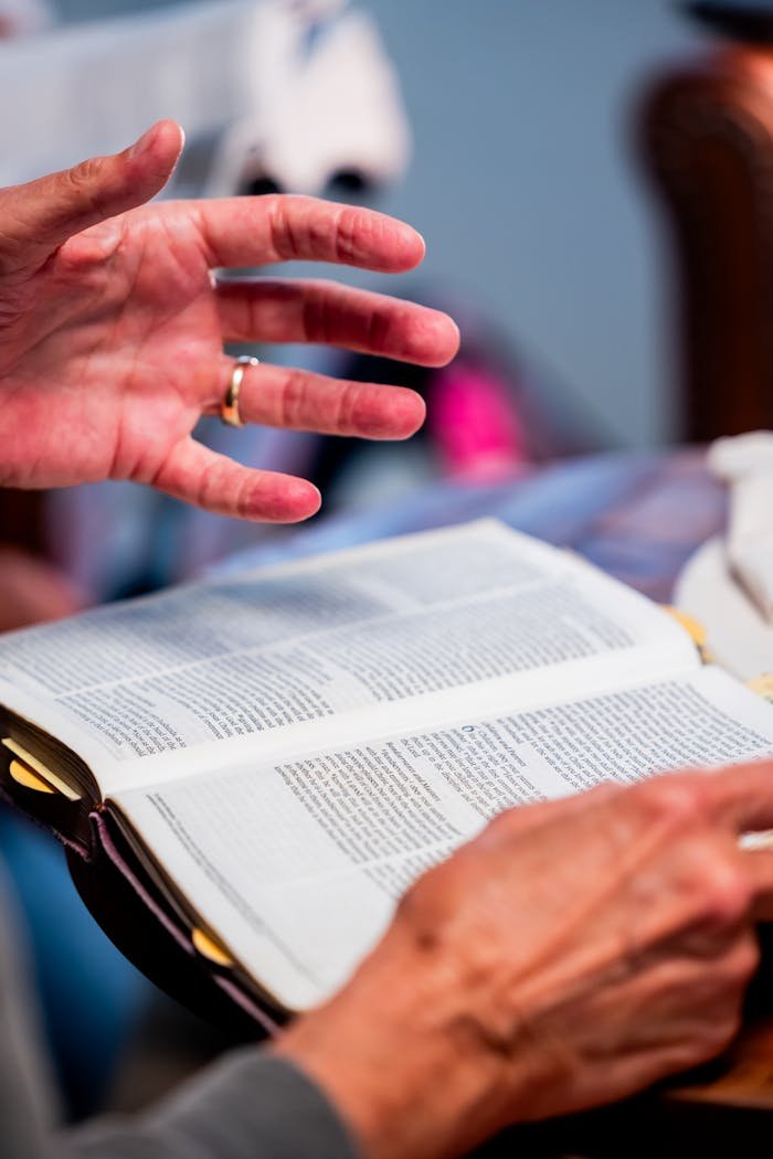 Close-up of hands engaged in Bible study at an indoor setting, promoting spiritual discussion.