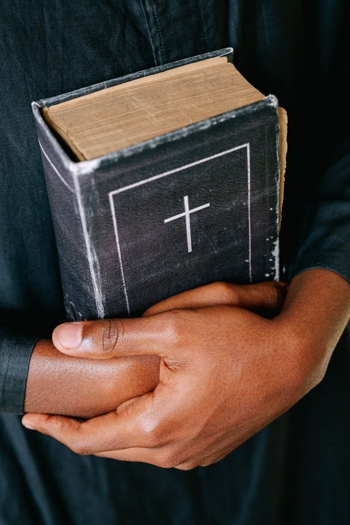 Close-up of hands holding a worn Bible featuring a cross symbol, symbolizing faith and spirituality.